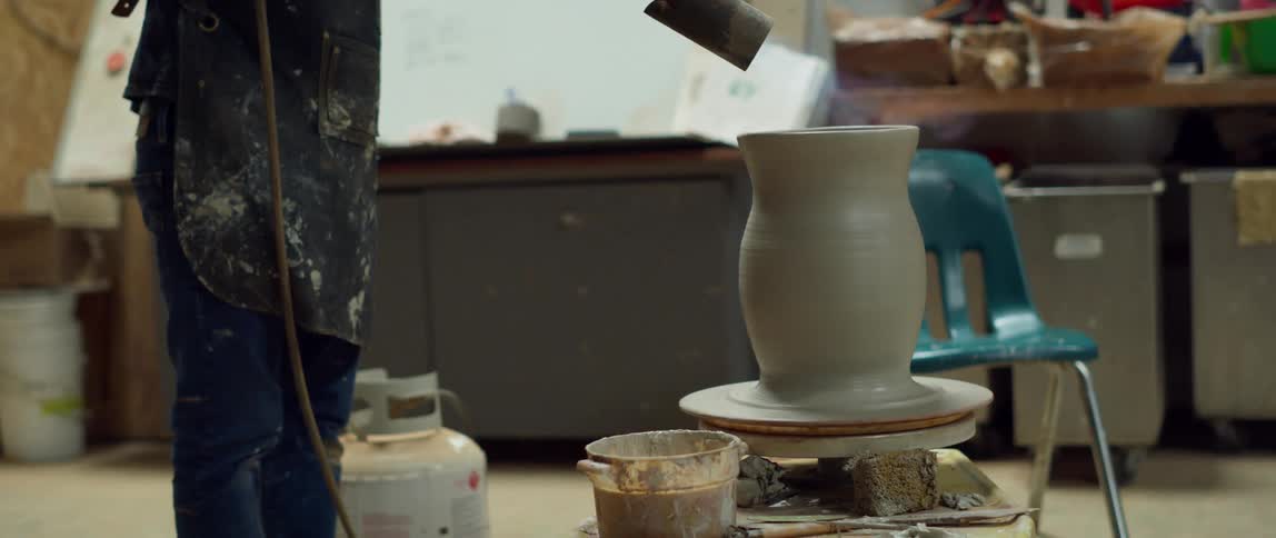 A pot is on a pottery wheel and someone is firing it with a torch