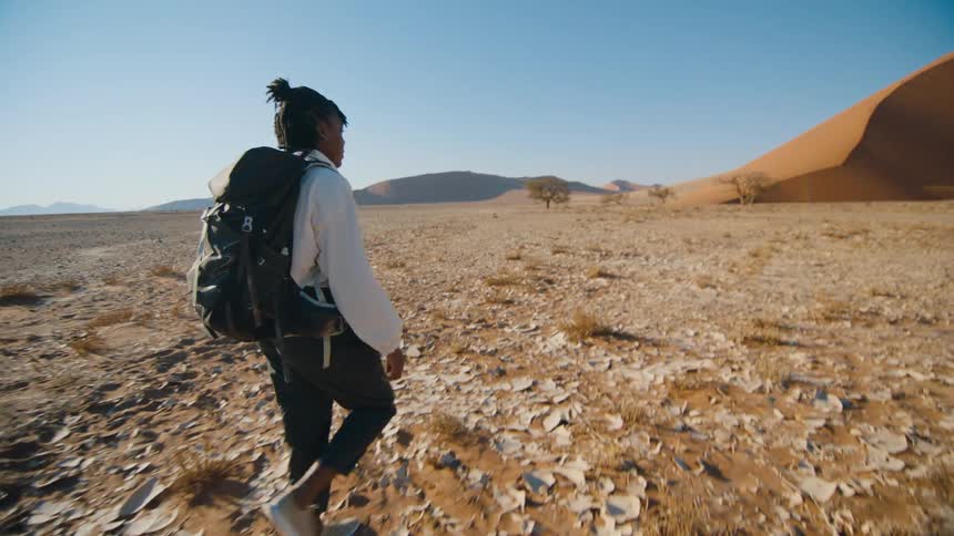 A black woman wearing a backpack is walking through the desert