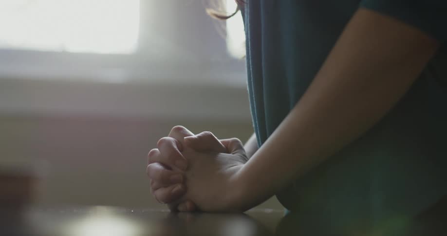 Someone is standing with their hands clasped together as if they are praying