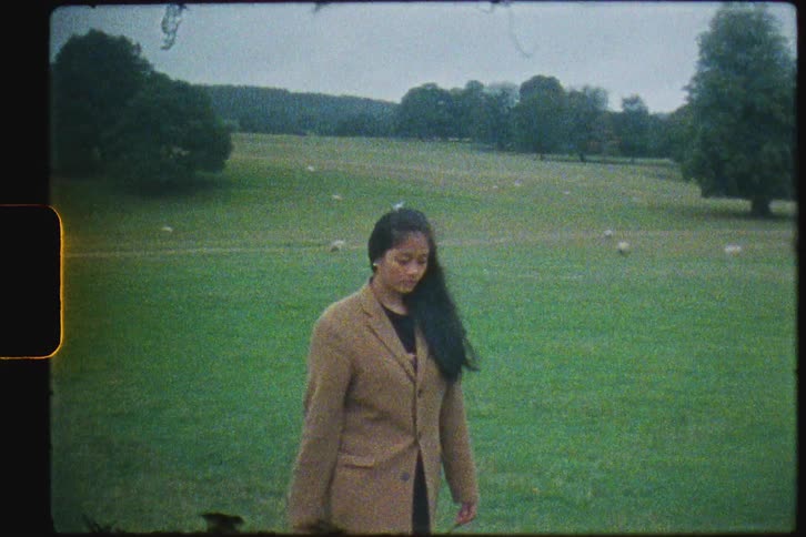 A woman in a long coat walks through a vast field during the day