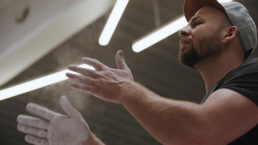 Man with white powder on his hands and wearing a baseball cap claps his hands together causing white dust