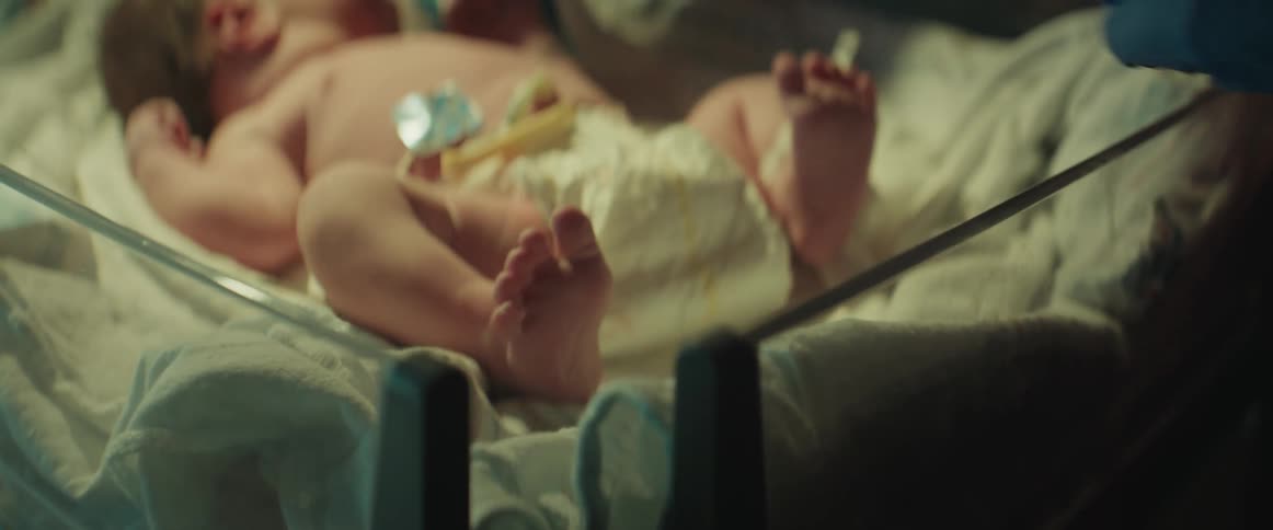 Newborn baby feet lie in a hospital bassinet as someone wearing blue gloves examines it