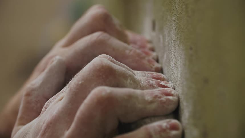 Close up of the fingers of a person holding a rock climbing hold covered in chalk