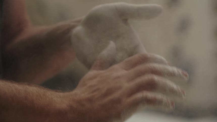 A man claps his chalk covered hands together while standing indoors