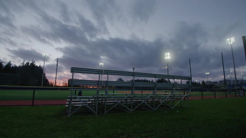 Benches over the green grass near a baseball field at sunset
