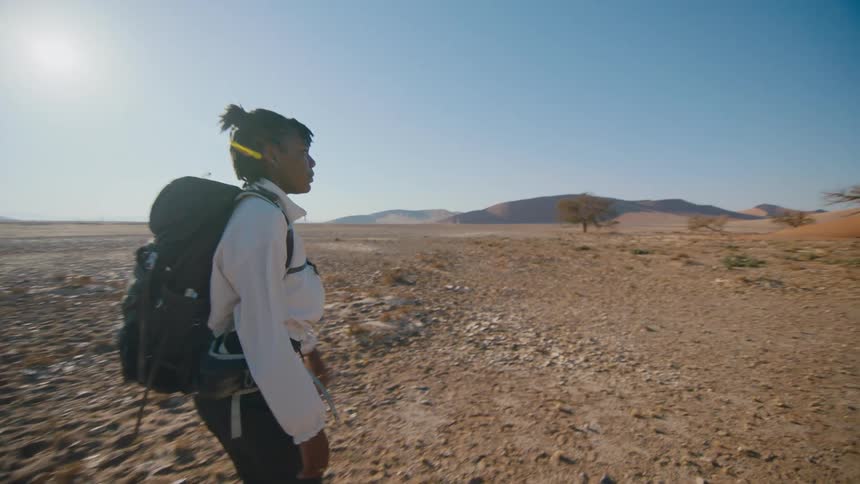 Young woman carrying a backpack walking on the desert near the sand dunes