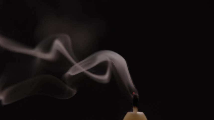 A burning candle in a dark place is blown out causing smoke to be emitted from the wick