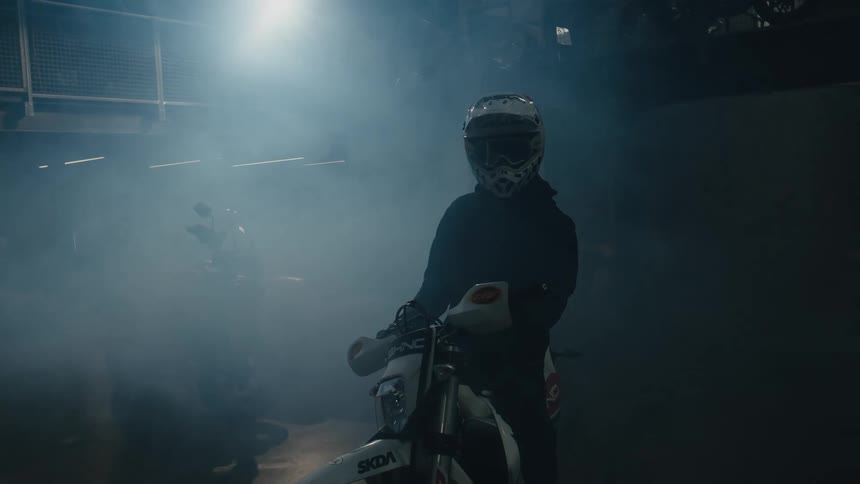 Biker with helmet and black jacket sits on motorcycle in misty room
