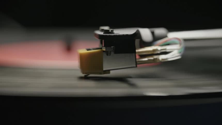 A turntable arm and needle as a record album spins on the player