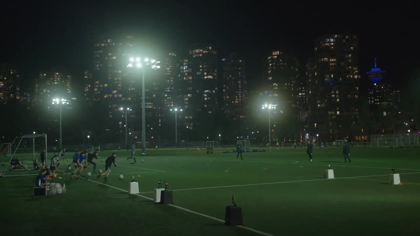 Soccer players kick balls back and forth during practice at a field with views of downtown
