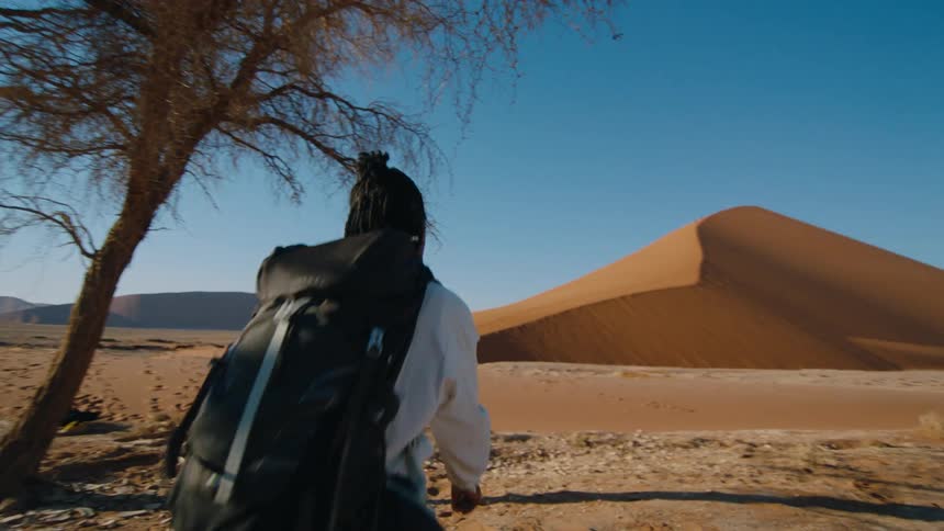 Woman with dreadlocks white shirt green pants and shoes walks across the desert