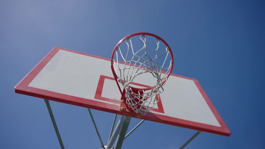 Red and white outdoors basketball hoop against a bright blue sky