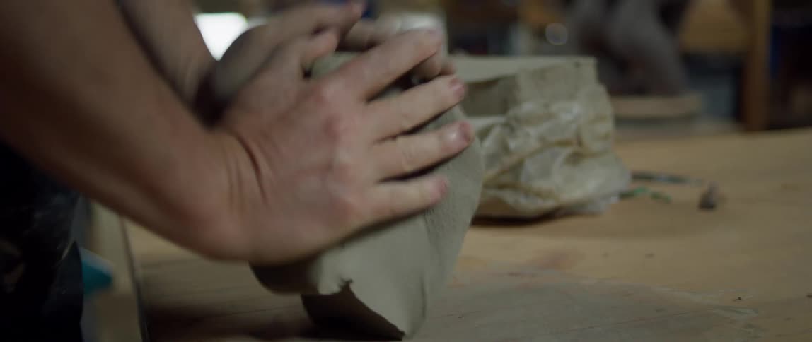 A man pounds and kneads half of a clay block on a worktable