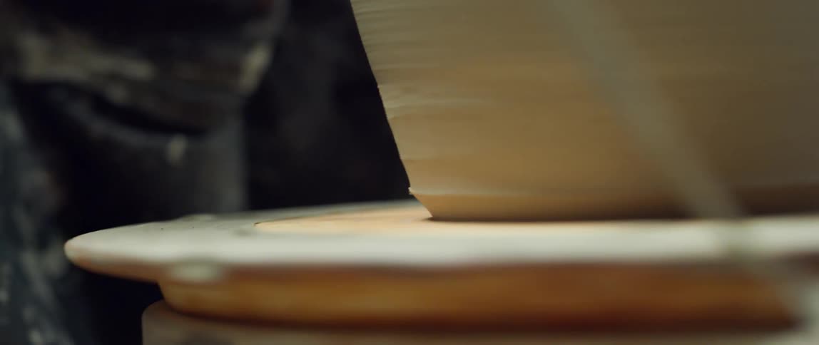 Someone is using a knife to shape the bottom of a pot on a pottery wheel