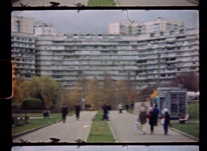 People walking in a city park with a large building complex behind them