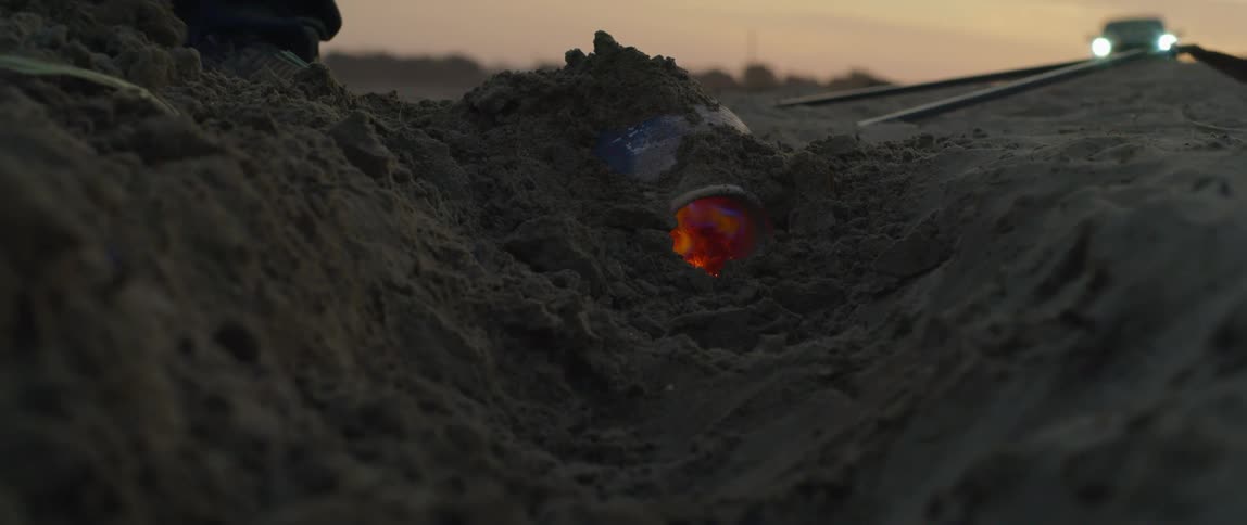 A man shovels dirt over a vase with fire in it