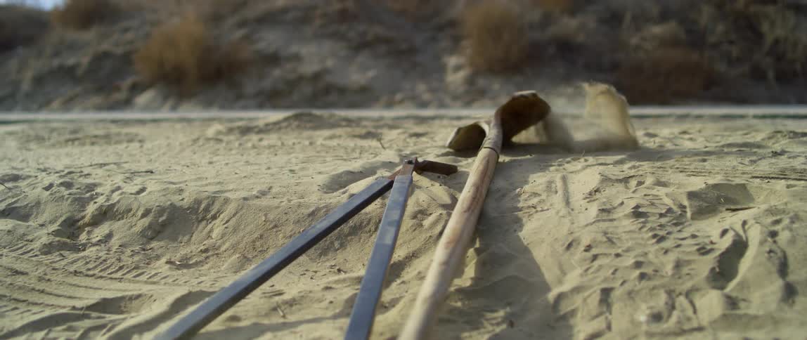 Bolt cutters and shovels land on the ground in the desert