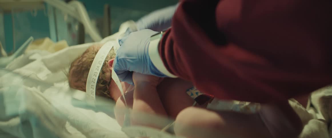 Nurse with red scrubs and gloves measures newborn baby in incubator