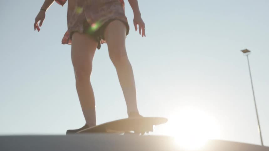 Woman with ponytail pinl shirt shorts and black shoes does skateboarding in skatepark