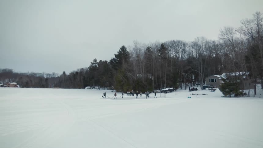 A group of people are outside playing hockey on a winter day and others are watching