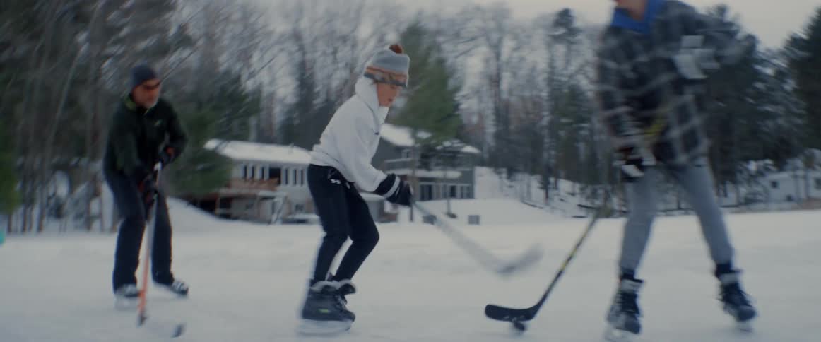 Young friends playing ice hockey on an open space outdoors with a few houses around with one player almost scoring a point