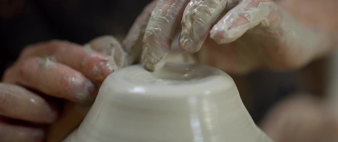 Fingers shape the wet clay spinning on a pottery wheel