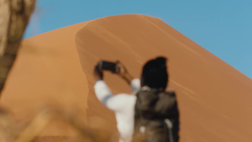 Person walks up to sand dune and takes a photo with smart phone