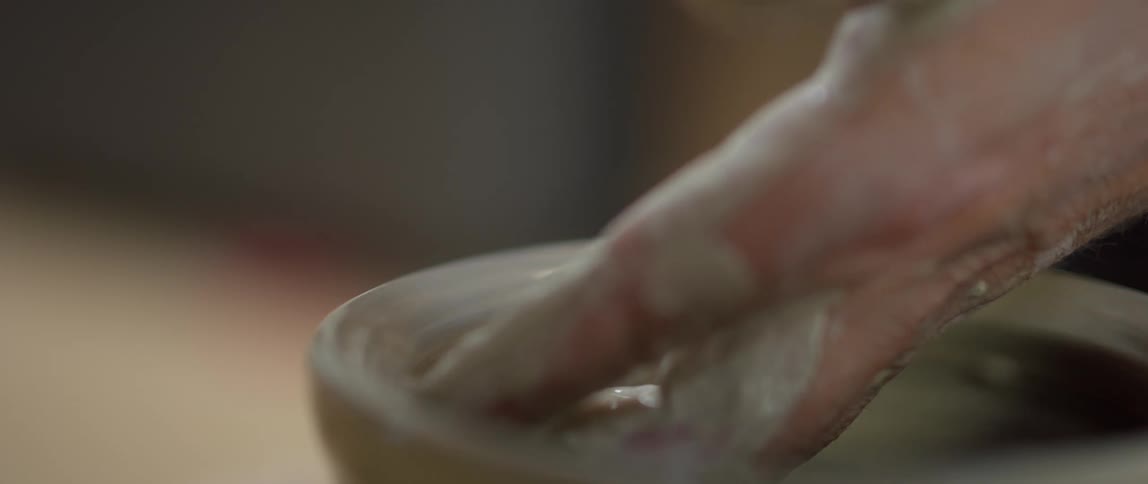 A man drips water on pottery as it spins