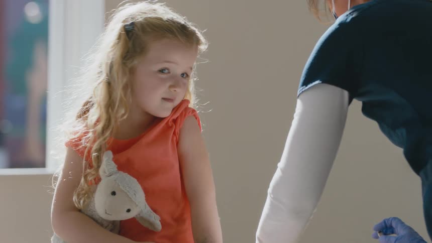 Female doctor gives a shot to a little girl that is holding a stuffed toy