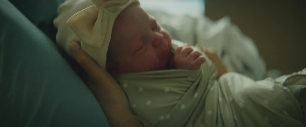 Mother holds a newborn baby that is wearing a hat with a big bow on it