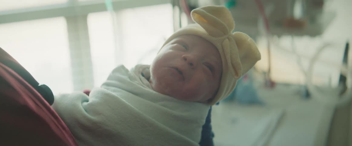 Nurse with red scrubs holds new born baby wrapped in blanket with yellow hat