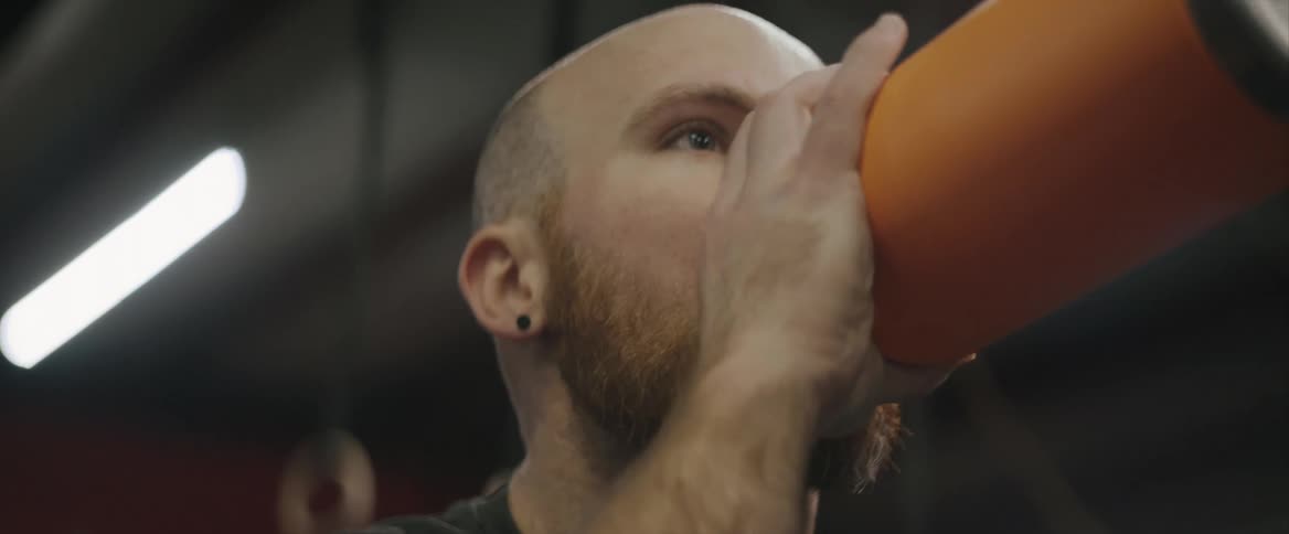 A man is indoors at the gym drinking a water bottle