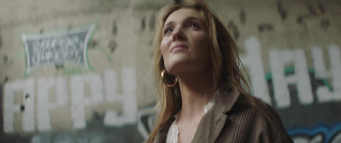 Young blonde woman standing in front of a wall filled inside an abandoned building