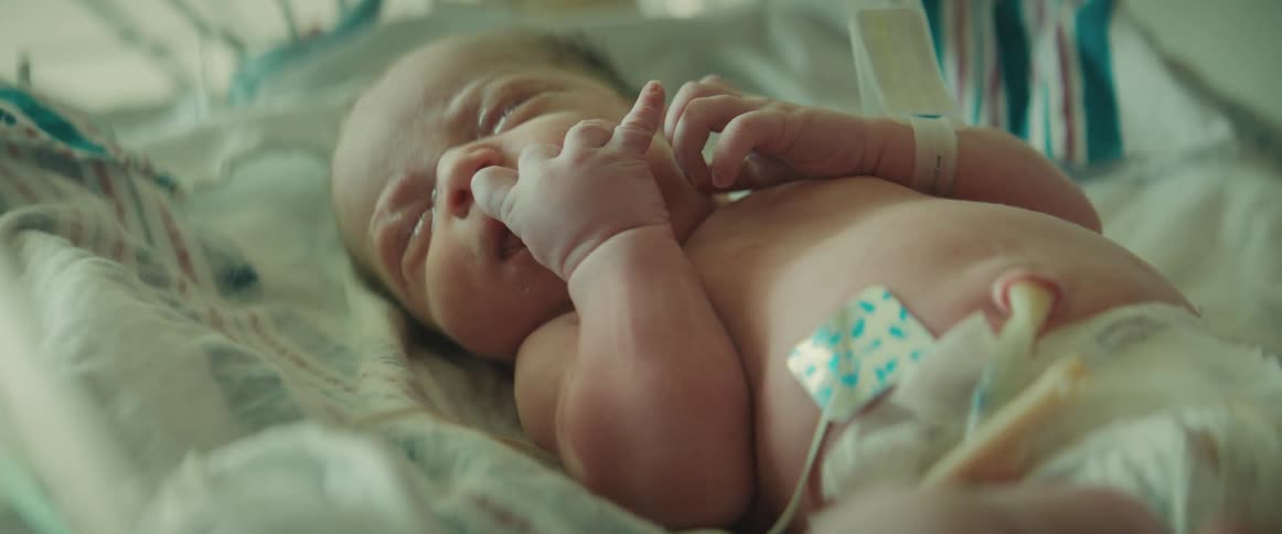 Newborn lies in crib in hospital nursery with sensors attached