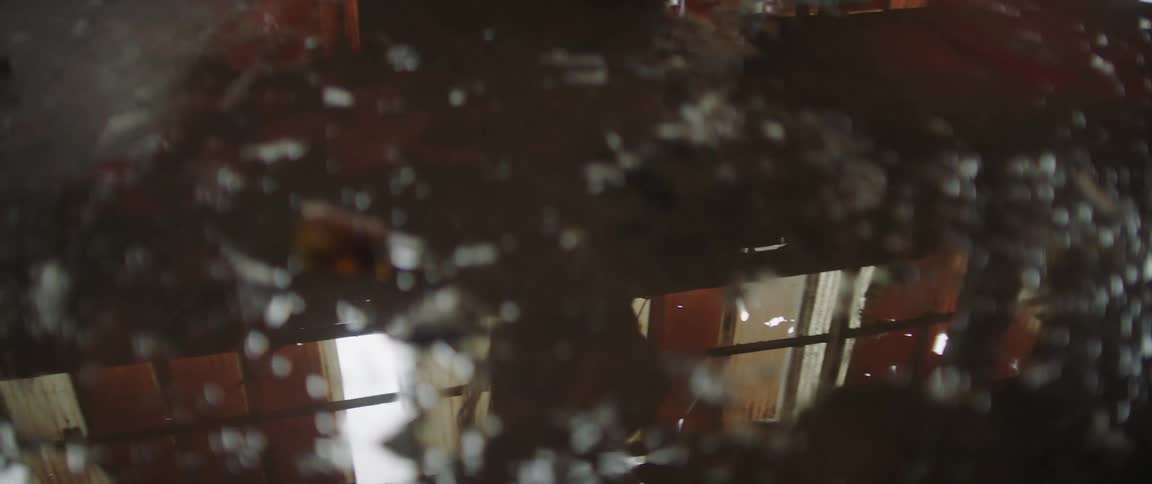 View through a window covered with water droplets of someone walking past windows with curtains on them
