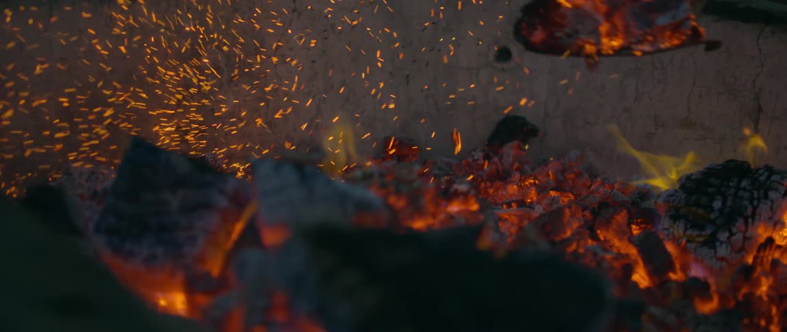 Someone uses a shovel to move burning wood and embers