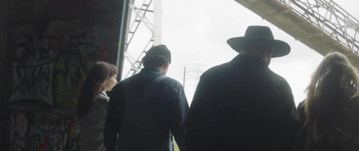 People are walking under a spray painted underpass and towards a bridge