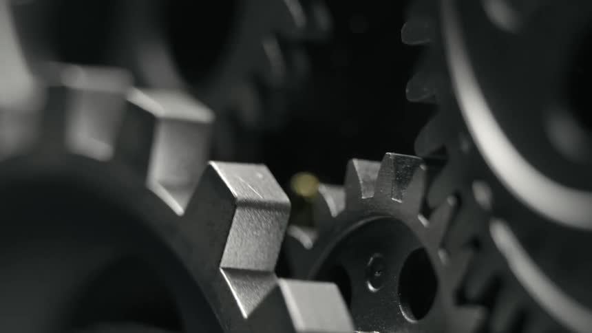 The teeth of rotating metal cogs pushing gears in opposite directions