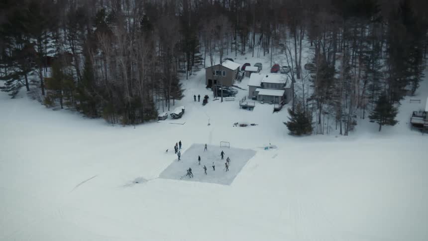 A group of people play ice hockey on a patch of ice in a rural area on winter day