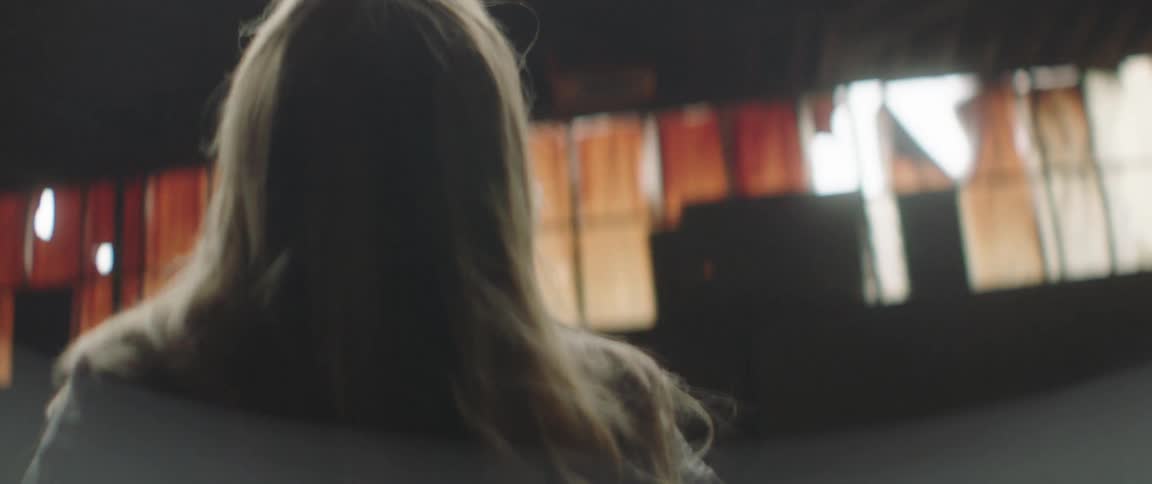Young blonde woman standing in front of a wall inside an abandoned building looking up