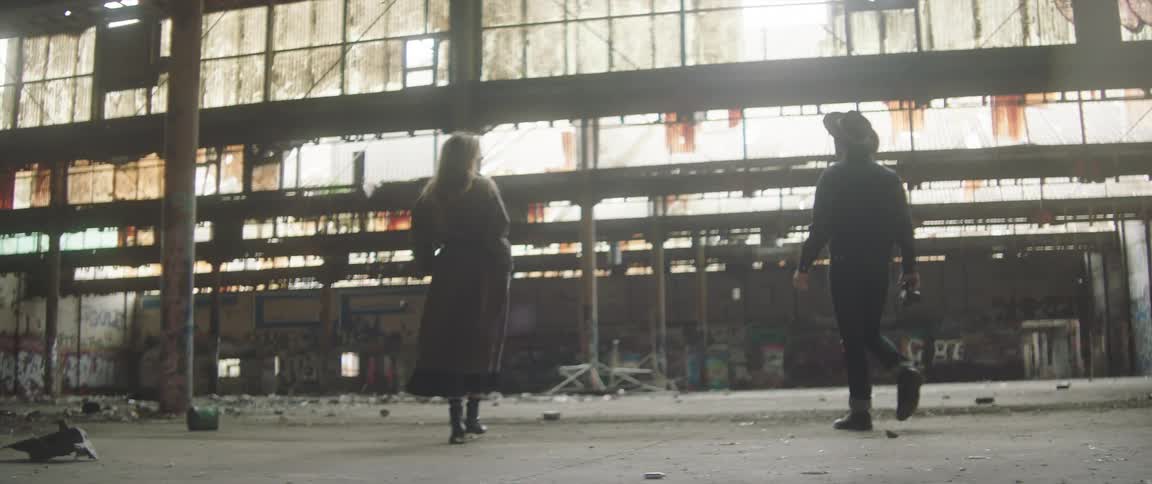 Man carries a camera as he walks in a derelict building with a woman