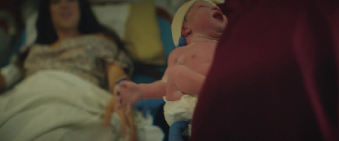 A nurse carrying a crying newborn baby to her mother who is in the hospital bed