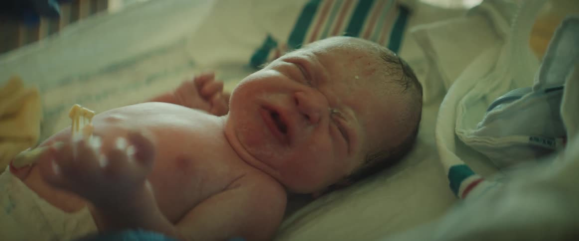 Nurse with red scrubs and blue gloves puts newborn baby in incubator