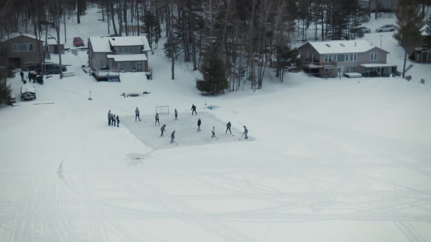 Group of people playing hockey on a field over a frozen lake near houses in the forest