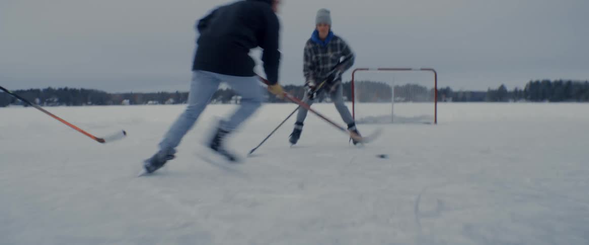 Young friends playing ice hockey on an open space outdoors during a cold day when one of them accidentally falls on the ground