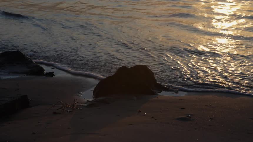 The lake waves roll into the rocks on the sandy beach
