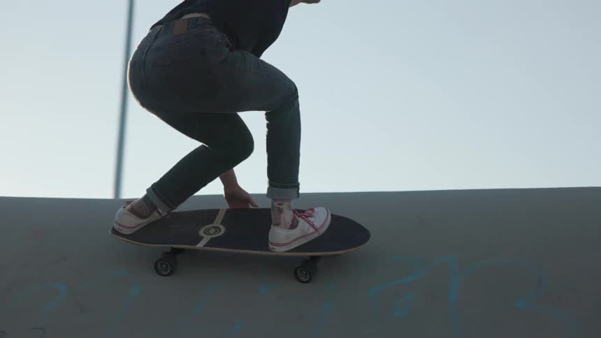 Skateboarder rides board along side of bowl decorated with graffiti
