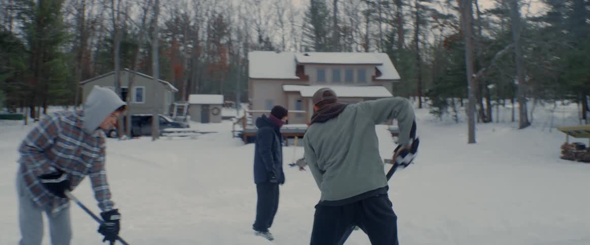 People watch as youth play ice hockey on frozen lake near houses