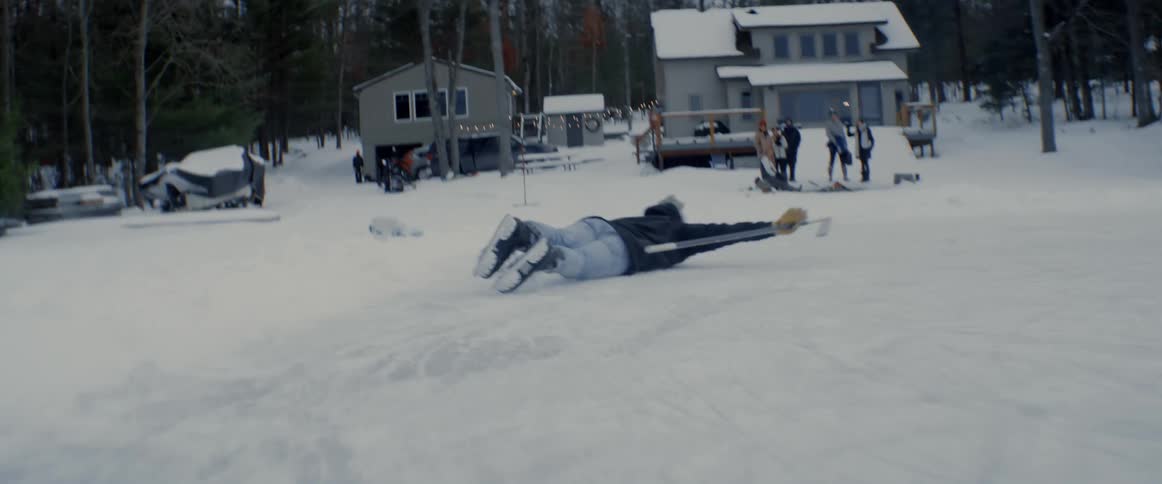 Man playing ice hockey on frozen lake celebrates then falls and slides with buildings in the background