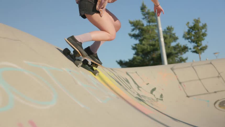 A womans shirts billows around her as she skateboards at a skate park on a bright sunny day